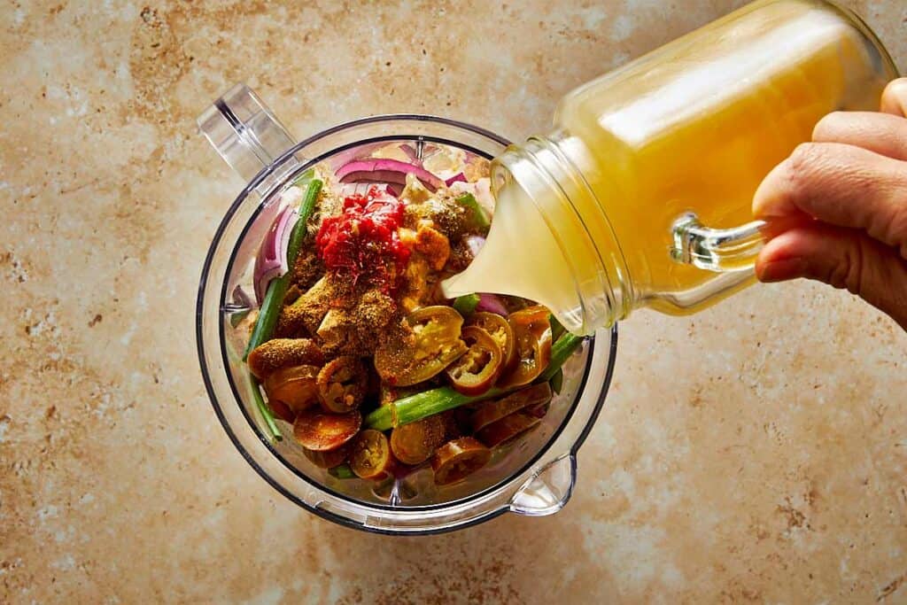 a blender jug with vegetables and liquid being poured into it