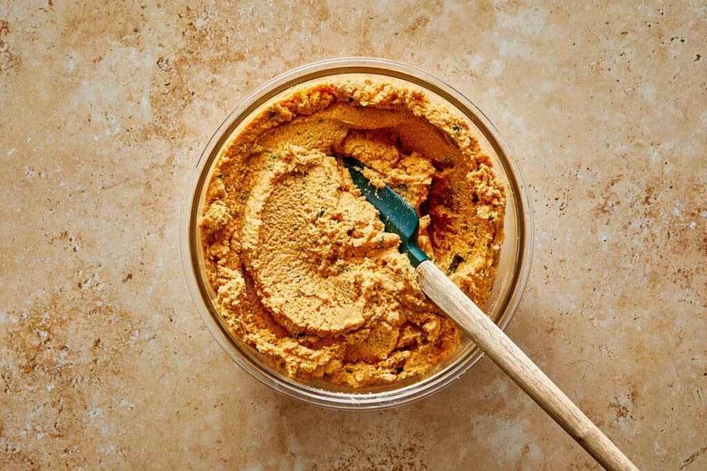 a mix of ingredients in a clear bowl being mixed with a wooden spoon