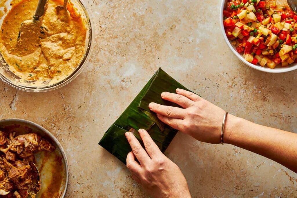 A large blue enameled pot containing several steamed banana leaf tamales arranged for serving