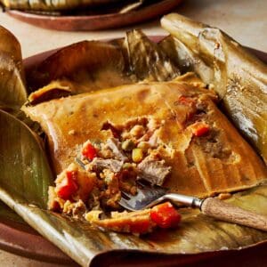 Top-down view of a turquoise Dutch oven filled with stacked tamales wrapped in banana leaves