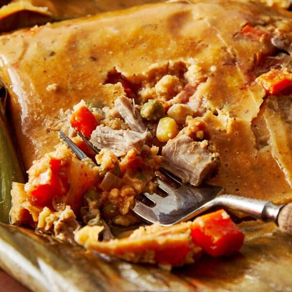 Top-down view of a turquoise Dutch oven filled with stacked tamales wrapped in banana leaves
