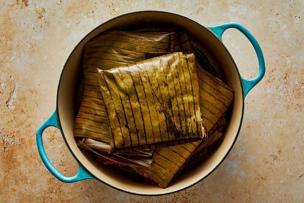 Top-down view of tamales wrapped in banana leaves stacked inside a teal Dutch oven