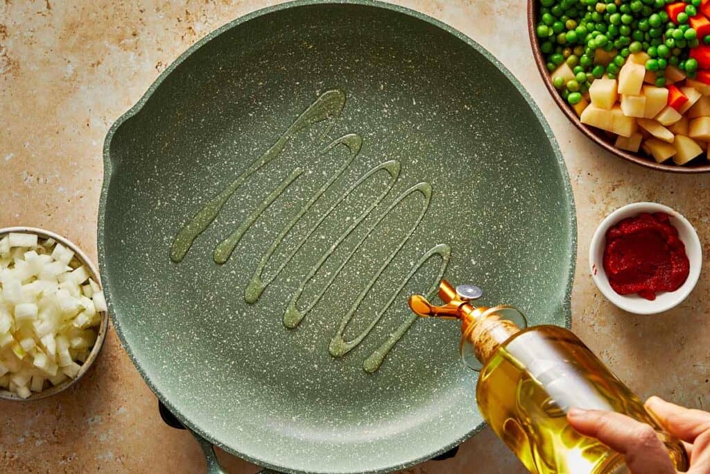 a green frying pan being poured into with olive oil