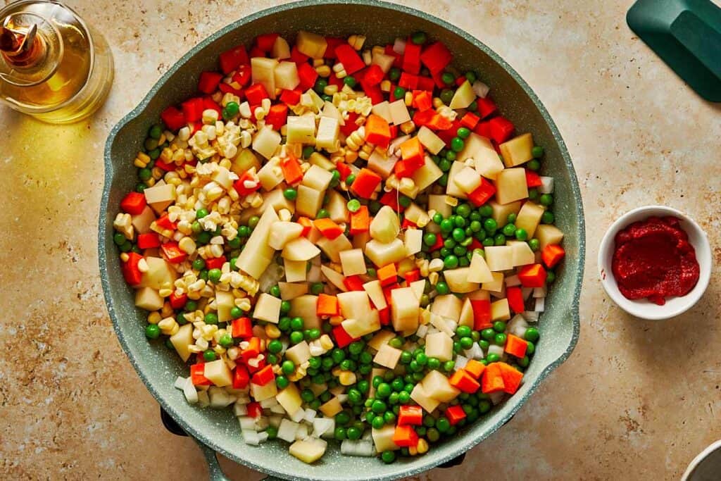 vibrantly colored vegetables chopped up into little cubs being mixed in a bowl with a wooden spoon