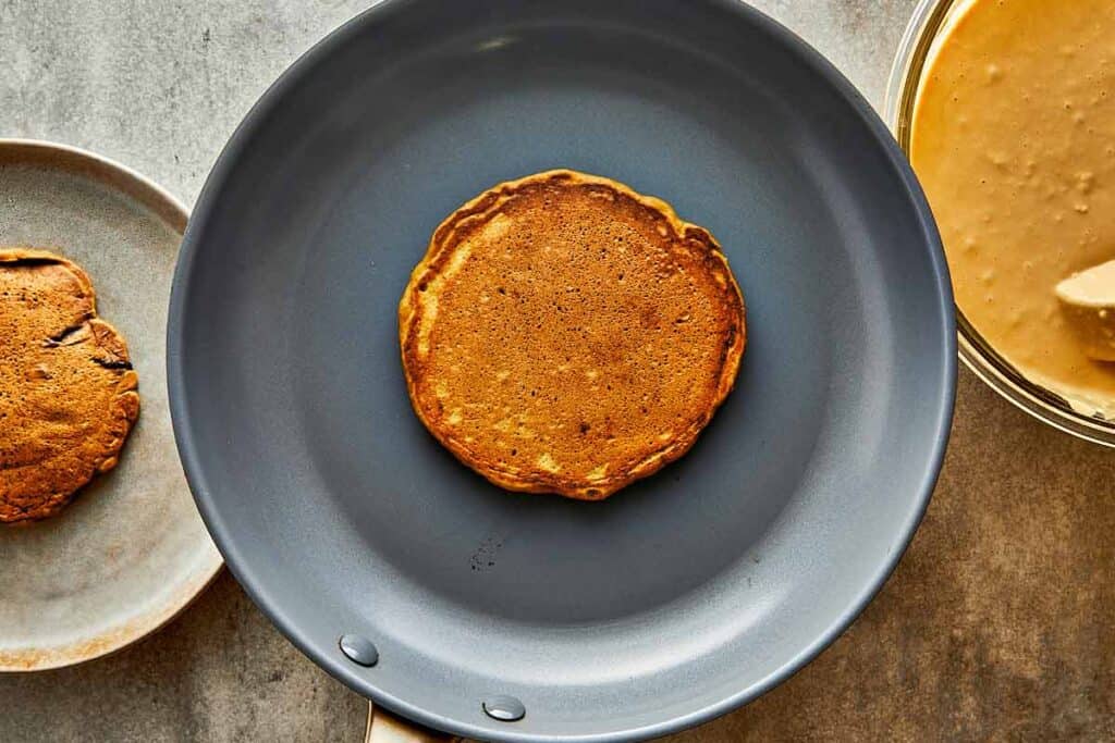 a dark pancake in a frying pan browned on the top and frying in a pan