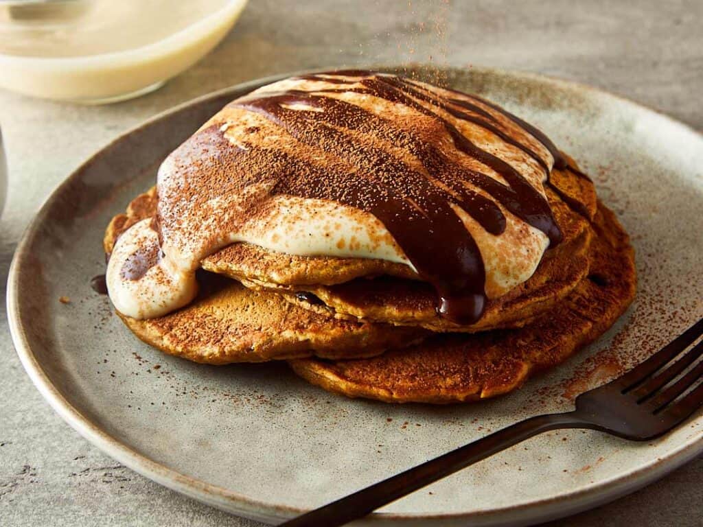 3 pancakes stacked one on top of another, side view, with what looks like greek yogurt on top and drizzling of chocolate coffee on top