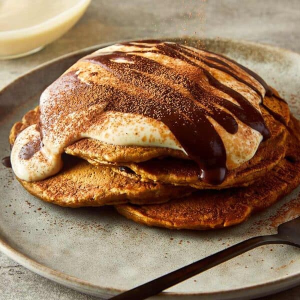 3 pancakes stacked one on top of another, side view, with what looks like greek yogurt on top and drizzling of chocolate coffee on top