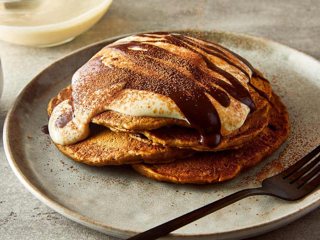 3 pancakes stacked one on top of another, side view, with what looks like greek yogurt on top and drizzling of chocolate coffee on top
