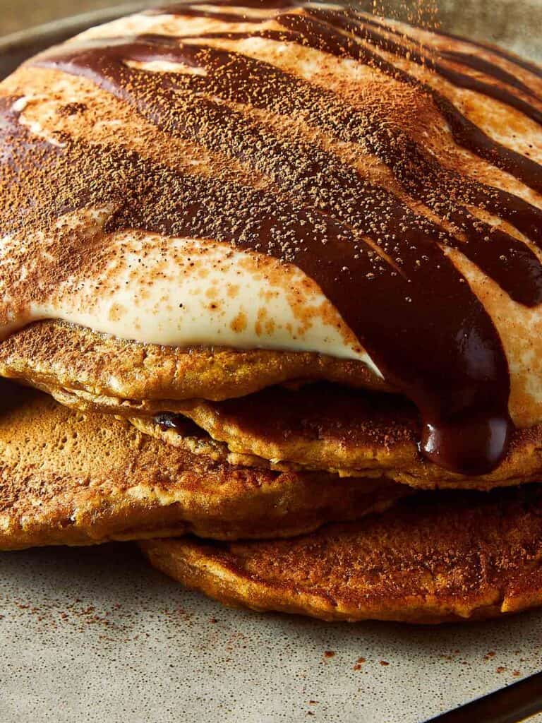 3 pancakes stacked one on top of another, side view, with what looks like greek yogurt on top and drizzling of chocolate coffee on top