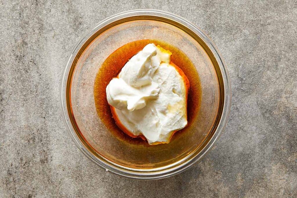 a top down shot of a mixing bowl made of glass on a counter top with a dollop of greek yogurt sitting in the bottom of the bowl.