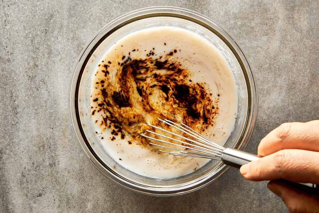 a glass mixing bowl with pancake mix inside and a spoon of coffee drizzled on top