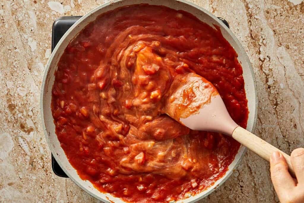 a top down view of a pan with a wooden spoon mixing a red sauce