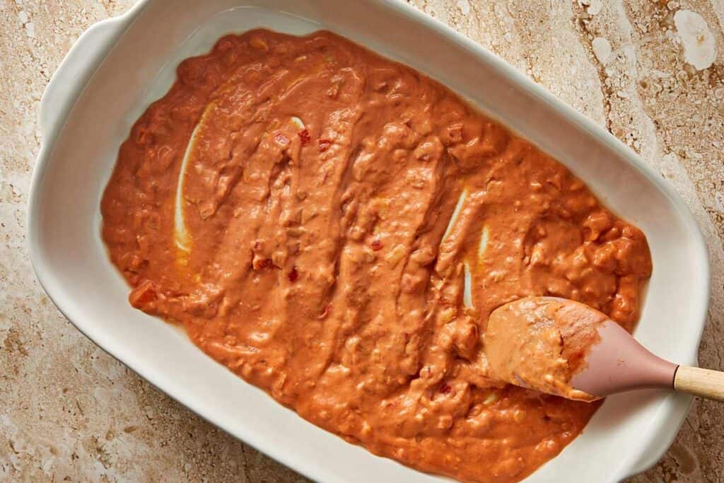 a orange what looks like creamy sauce in a backing dish, it's being spread over the base of the dish looking like a bed of sauce