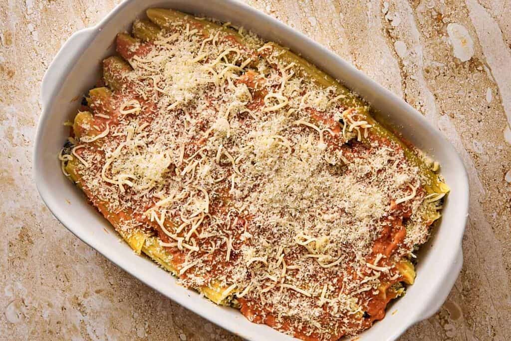 a top down shot of a dish filled with cannelloni and orange sauce on top with cheese sprinkled on top