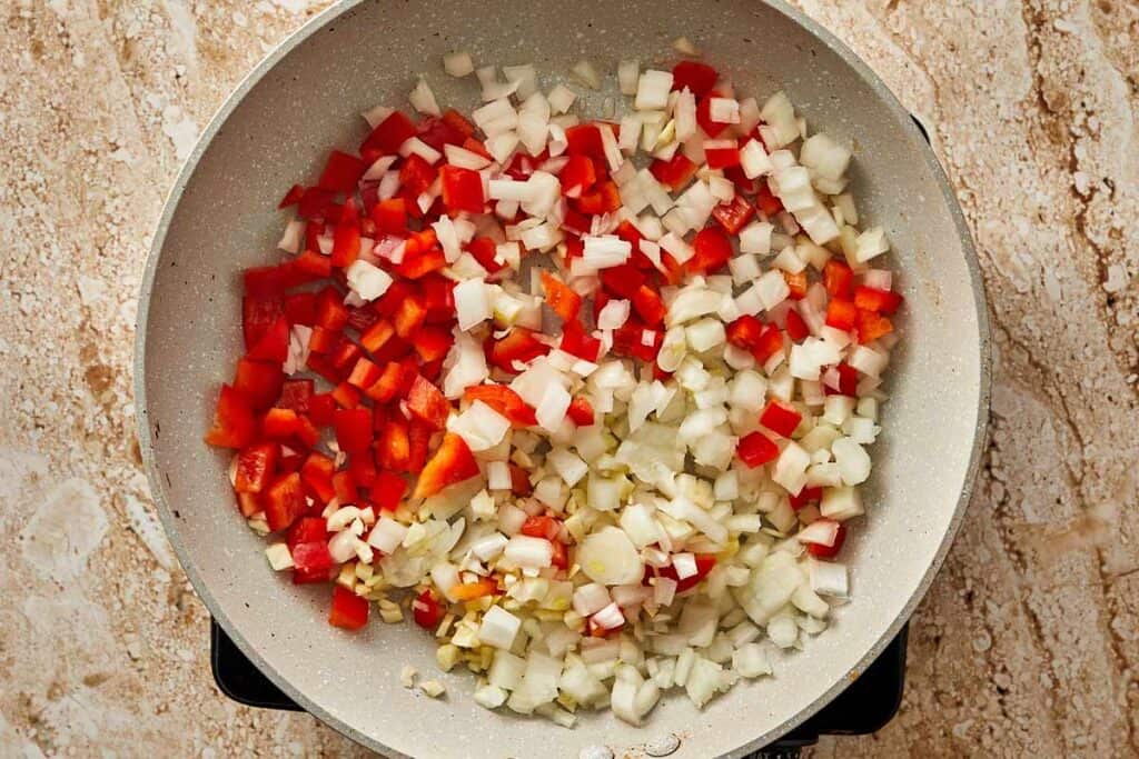 a top down view of a ceramic pan with onion diced, crushed garlic and diced bell peppers frying