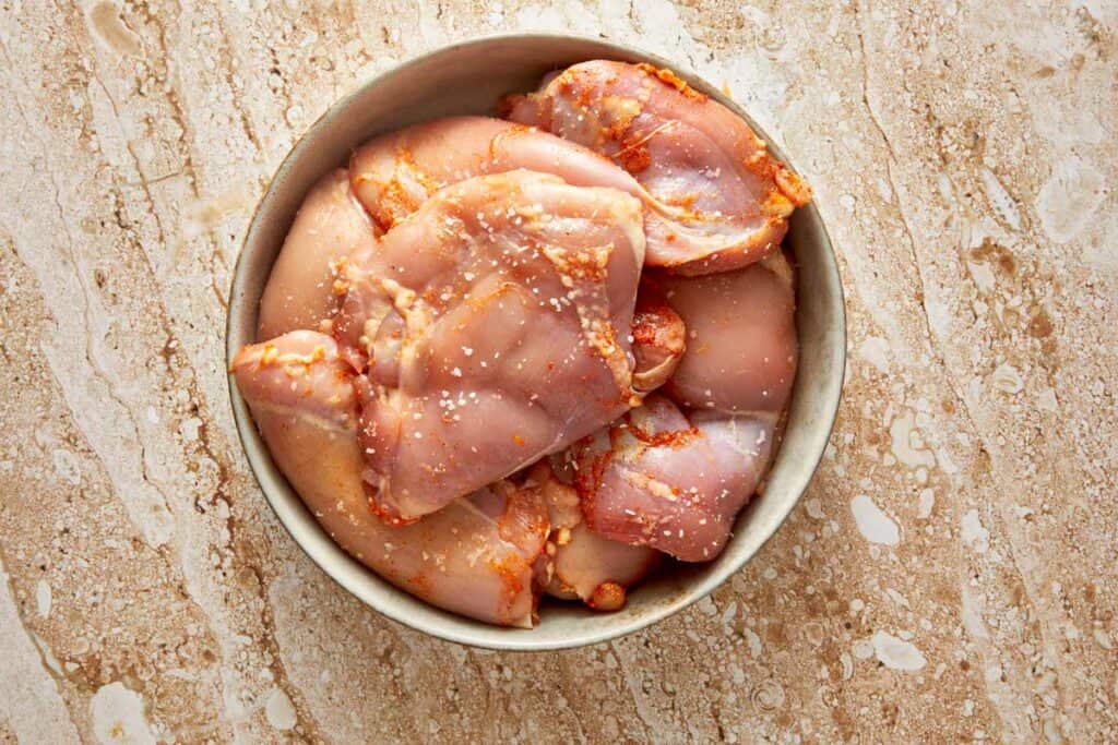 a top down view of a bowl sitting on a counter with raw chicken thighs coated in spices
