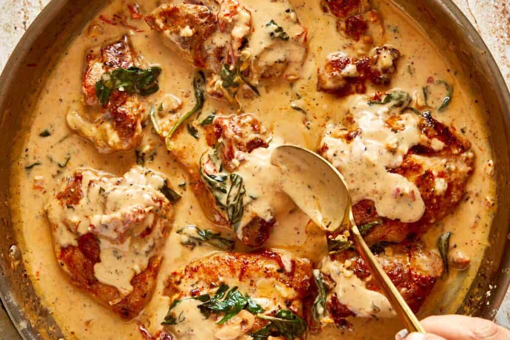 a close up shot with a spoon top down of a creamy brown sauce and golden baked chicken swimming in the sauce