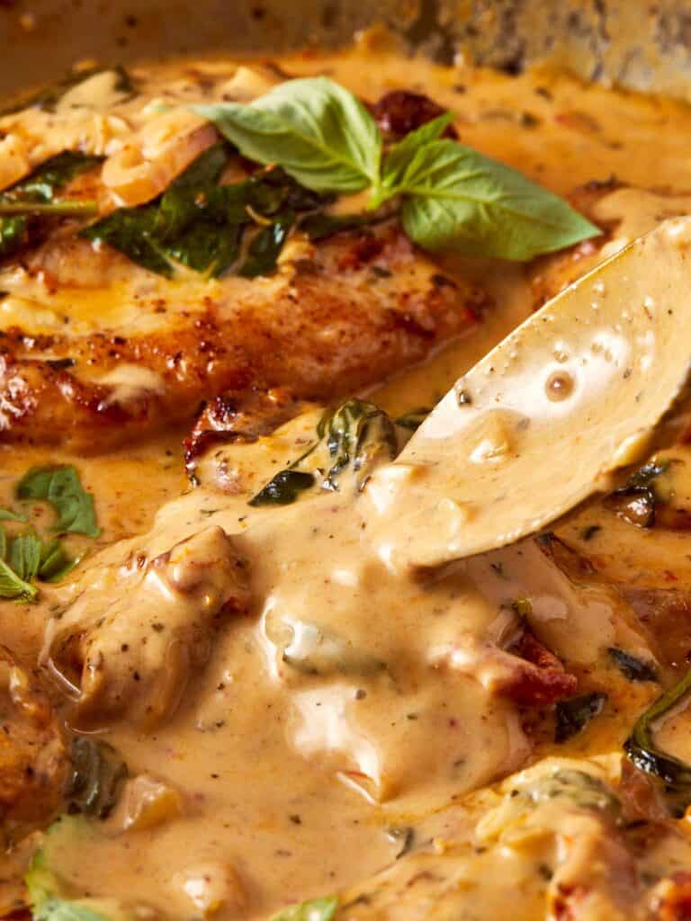 A gold spoon pouring chicken sauce on top of chicken thigh pieces with green leaves on top