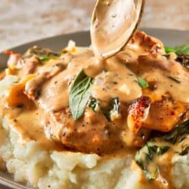 A side view of the tuscan Chicken on a bed of mashed potatoes on top of a green plate with a gold spoon pouring the sauce on top. - 13