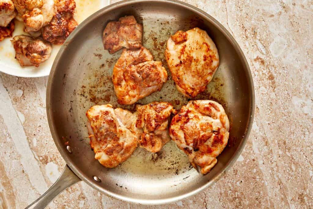 a top down view of a pan with chicken thighs cooking and browing