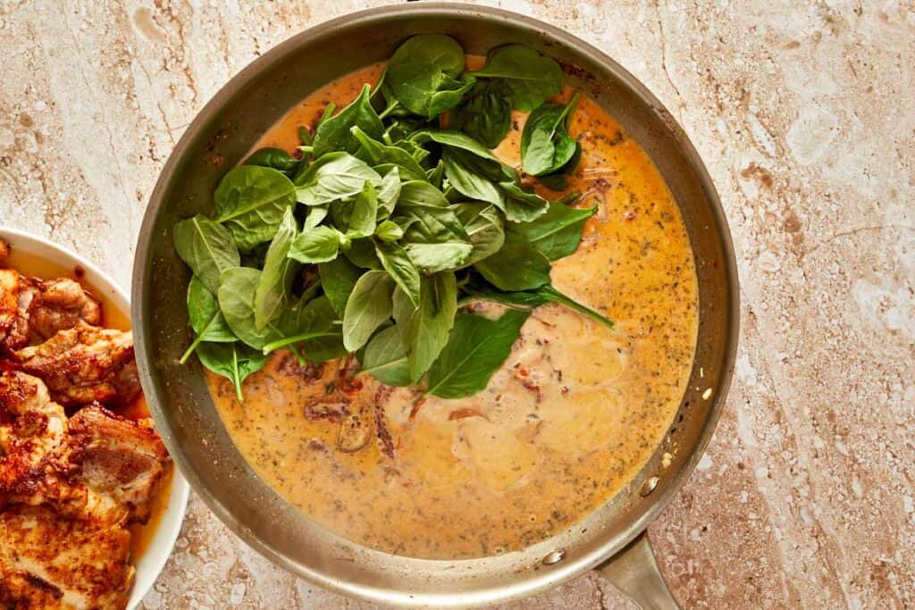 a top down shot of a bowl of creamy sauce with spinach on top getting ready to mix