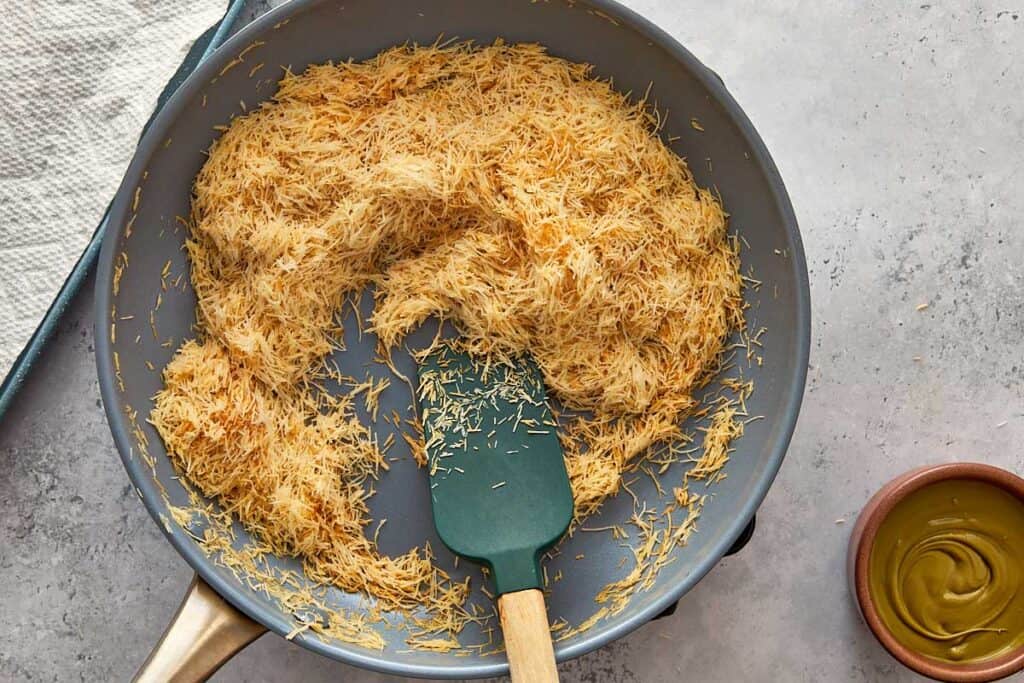 toasted kadaïf being mixed with a wooden spoon in a saucepan
