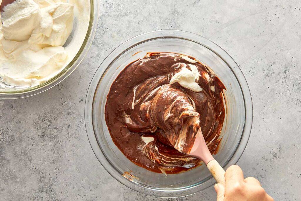 mixing the chocolate mix with the soft peaks of cream in a glass bowl with a wooden spoon.