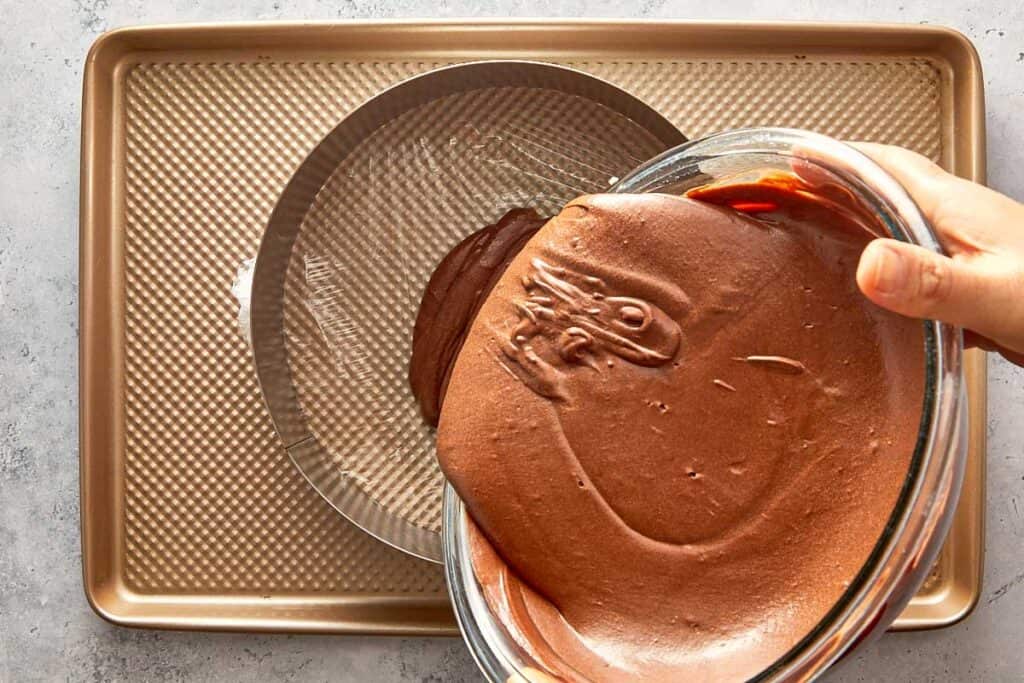 pouring the chocolate mousse mix into a cake ring with a plastic wrap on the base