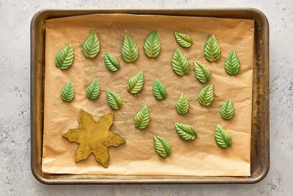 a large chocolate star covered in golden edible glitter and green chocolate leaves sitting on a baking tray ready to decorate the cake