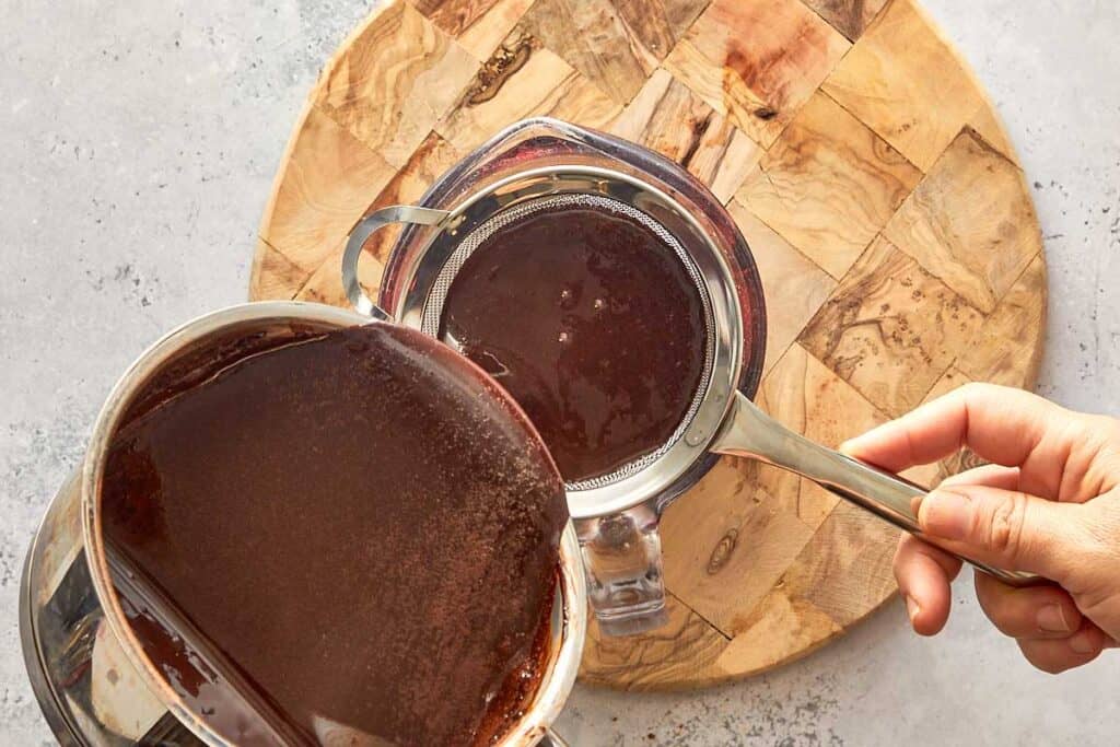 thicker darker chocolate being poured into a glass jug that can be used to pour on top of the cake