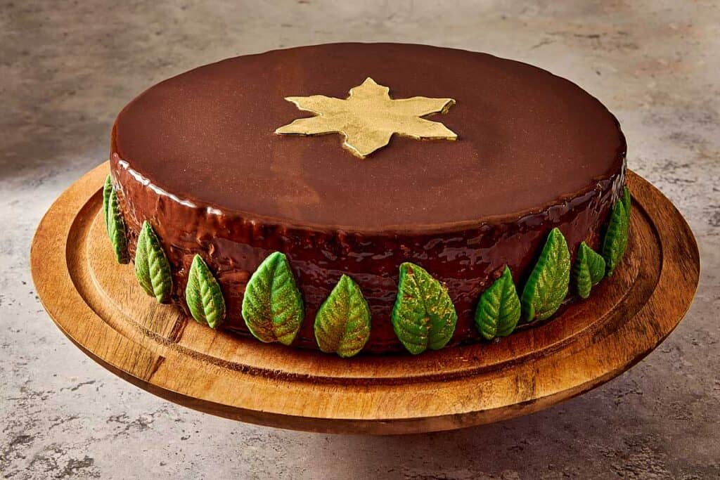 a round glazed chocolate cake side view sitting on a cake tray decorated with green leaves and a golden star on top