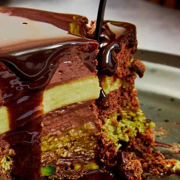 Delicious slice of dubai chocolate cake with chocolate glaze being poured on a wedge that has been cut out, you can see 4 distinct layers of cake