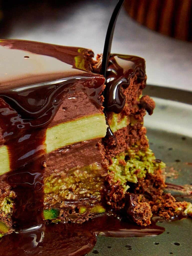 Delicious slice of dubai chocolate cake with chocolate glaze being poured on a wedge that has been cut out, you can see 4 distinct layers of cake