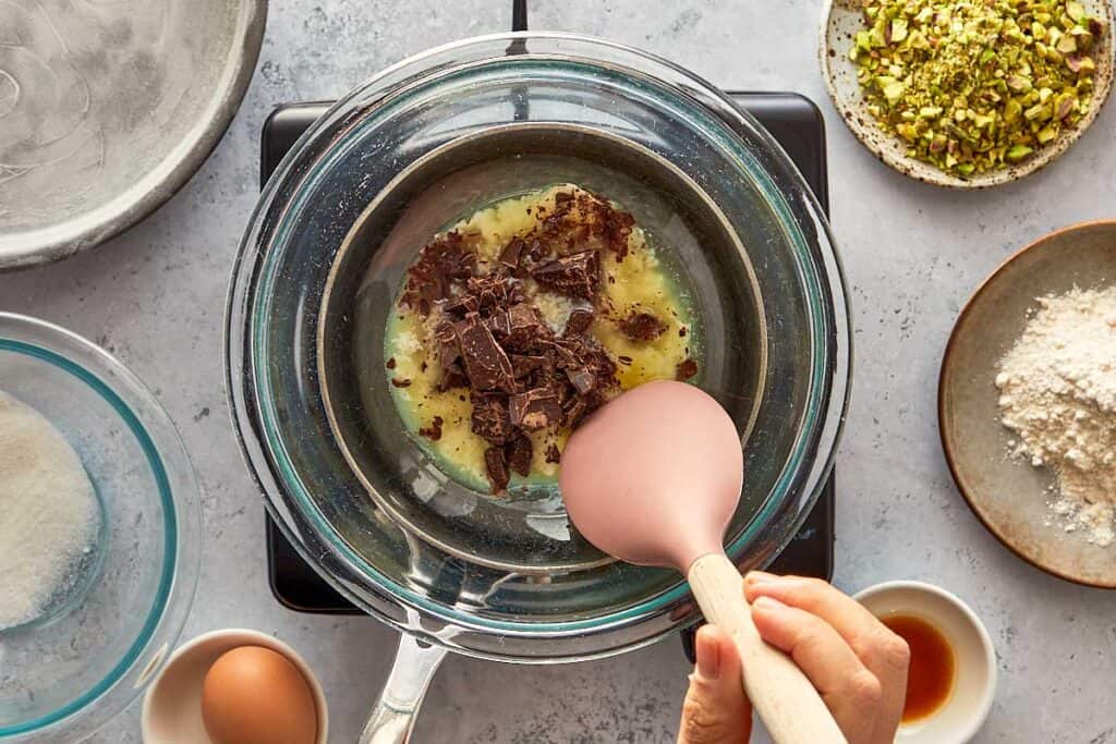 top down view of a double boiler with melting chocolate and butter mixing with a wooden spoon