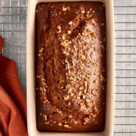 a top down view of banana bread baked in a rectangular loaf pan resting on a wire tray cooling, the banana bread is facing top to bottom - 13