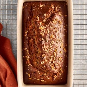 a top down view of banana bread baked in a rectangular loaf pan resting on a wire tray cooling, the banana bread is facing top to bottom
