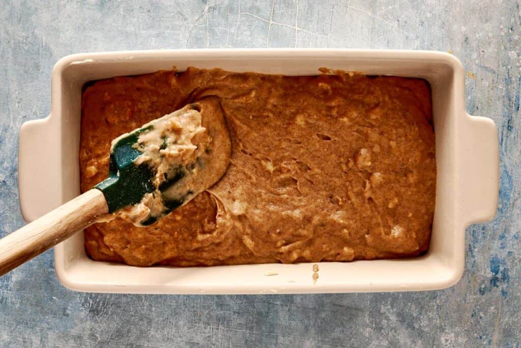 a top down view of a green spatual filling a rectangular loaf pan which is lined with parchment paper - 9