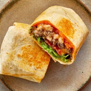 a top down shot of two halves of cheeseburger wrap with meat melted cheese and sauce close up resting on a chopping board