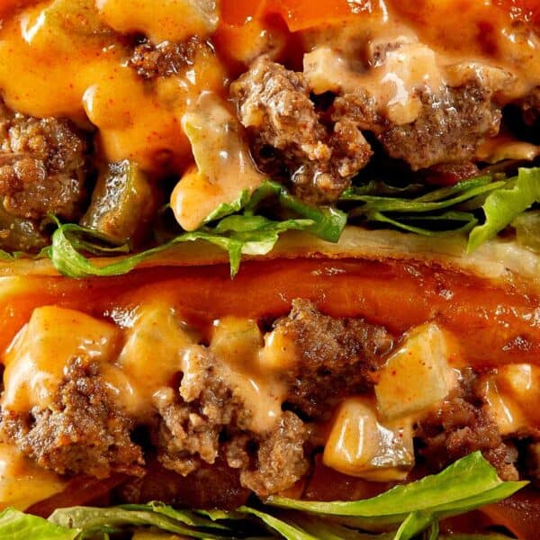 a side view of two halves of cheeseburger wrap with meat melted cheese and sauce close up resting on a chopping board