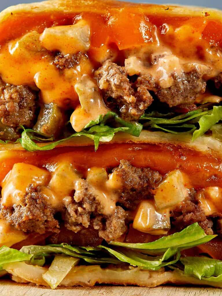 a side view of two halves of cheeseburger wrap with meat melted cheese and sauce close up resting on a chopping board