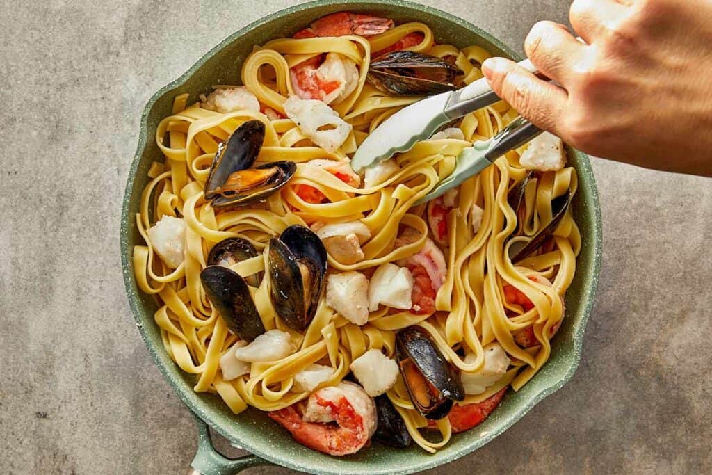 a top down shot of a hand holding tongs picking up pasta and seafood - 12