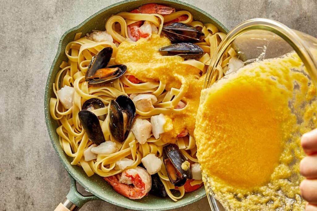 a pan of seafood and pasta and a bowl of liquid egg or yellow being poured into the pan - 14