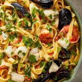 a top down view of a creamy seafood pasta dish in a green pan - 13