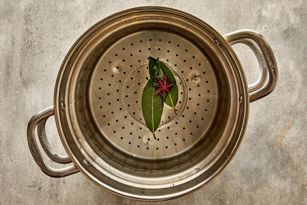 a top down view of a pasta sive with two bay leaves in the bottom of the strainer - 5