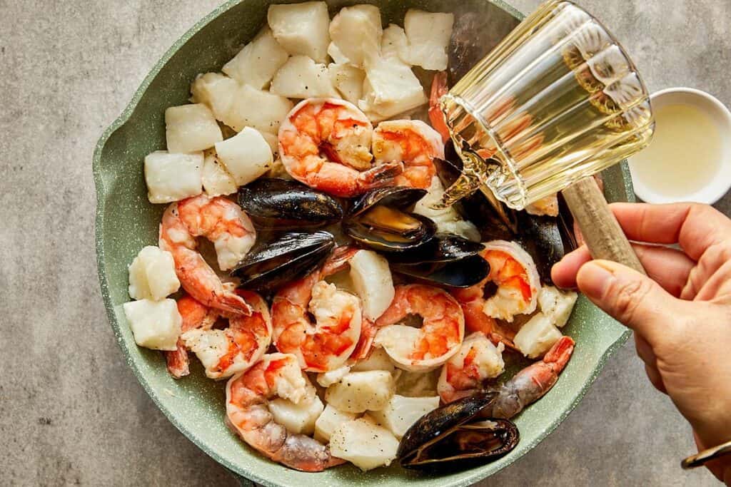 a pan full of seafood being cooked with a jug of water being added to the seafood. - 7
