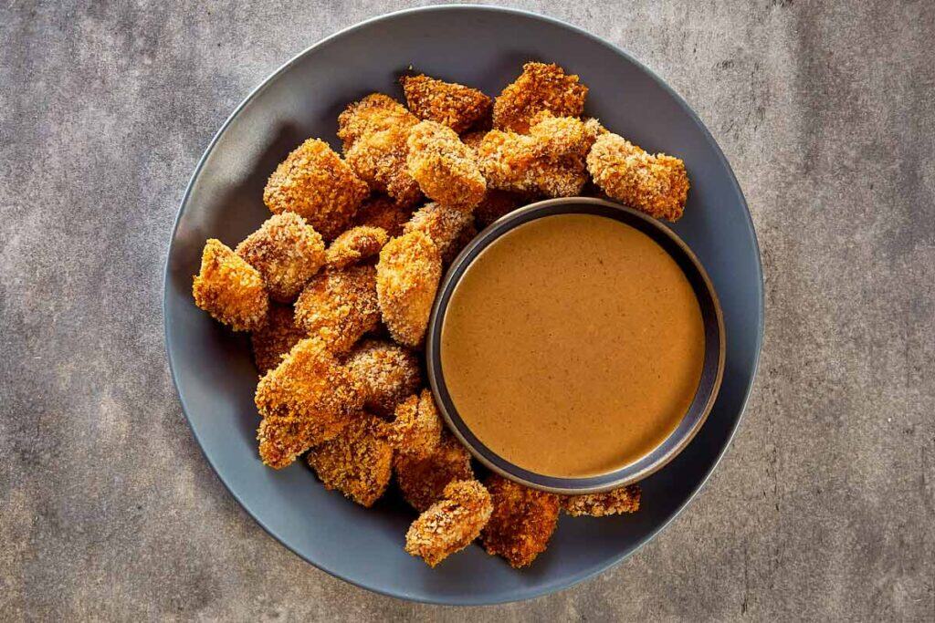 a top down view of chicken nuggets fully cooked on a plate and a bowl of sauce in the middle.