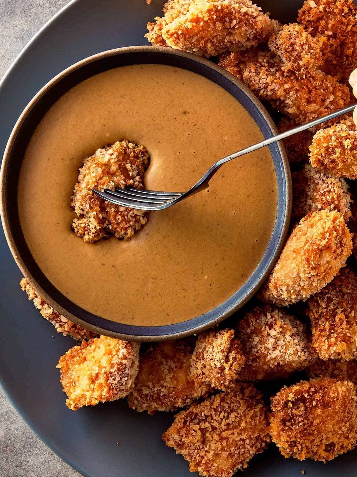 a top down view of chicken nuggets fully cooked on a plate and a bowl of sauce in the middle. with a fork dipping one nugget in