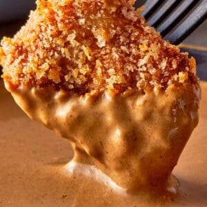 a side view of a single chicken nugget half dipped in sauce dripping hovering over a sauce bowl, held up by a fork, really close up shot