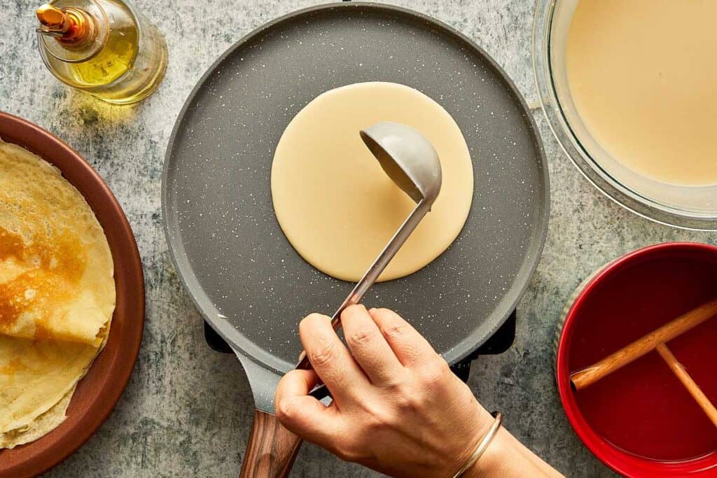 a top down view of a ladle of batter being poured into a crepe pan - 15