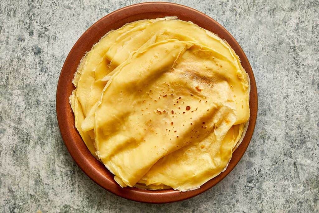 a cooked crepe sitting on top of a ceramic brown plate, the crepe is creased as it sits on the plate - 19